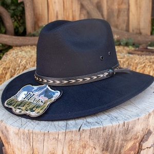 May include: A black felt cowboy hat with a braided leather band and a small feather accent. The hat has a tag that says "Hats" on it.