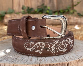 May include: A brown leather belt with a silver buckle and a white embroidered floral design.