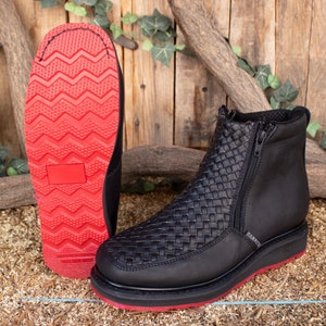 Może przedstawiać: Czarne skórzane botki z plecionym wzorem i czerwoną gumową podeszwą. Botki mają zamek błyskawiczny z boku i czerwoną gumową podeszwą.
