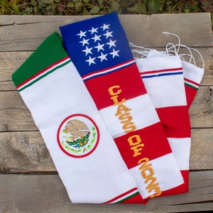 May include: A white, red, and blue graduation scarf with the text "Class of 2023" embroidered in gold. The scarf also features an embroidered Mexican flag with a green, white, and red design.
