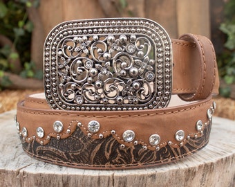 May include: A brown leather belt with a decorative metal buckle featuring a floral design and rhinestones. The belt has a black and brown patterned design and is embellished with clear rhinestones.