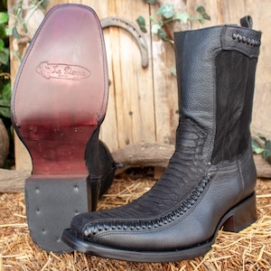 May include: Black leather cowboy boots with a square toe and decorative stitching. The boots have a textured vamp and a short, stacked heel. The sole of one boot is visible, displaying the brand "La Sierra Boots".