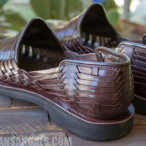 May include: A pair of brown leather sandals with a woven design. The sandals have a thick sole and are made of a soft, supple leather.