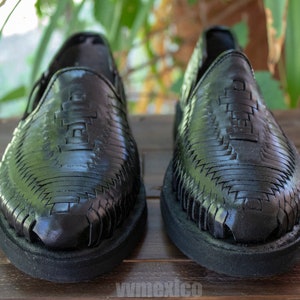 May include: A pair of black leather huarache sandals with a woven design. The sandals have a closed toe and a flat sole.