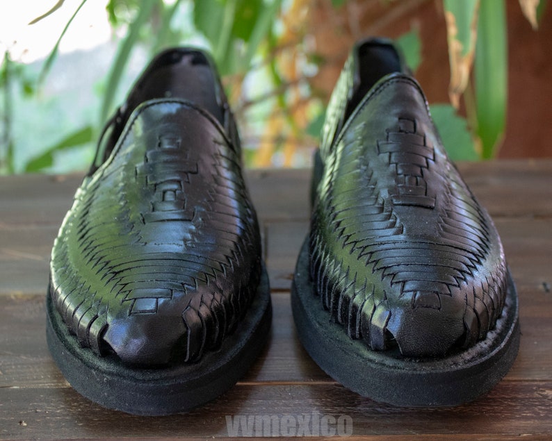 May include: A pair of black leather huarache sandals with a woven design. The sandals have a closed toe and a flat sole.