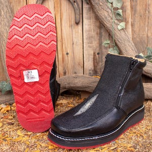 Może przedstawiać: Czarne skórzane buty z bocznym zamkiem błyskawicznym i czerwoną podeszwą z białym paskiem. Buty wykonane są ze skóry płaszczki i mają białe przeszycia wokół podeszwy. Etykieta rozmiaru na podeszwie wskazuje "26,5".