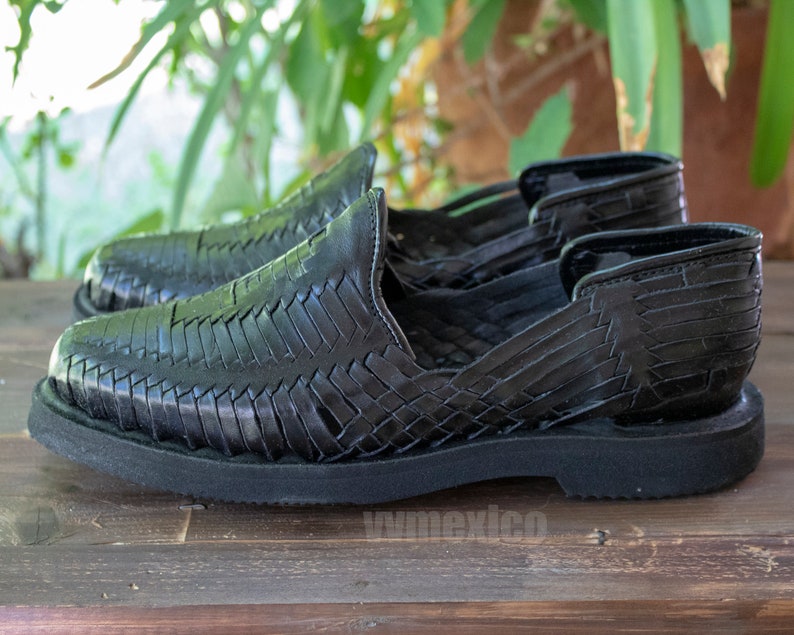 May include: Black leather sandals with a woven design and a thick black sole.