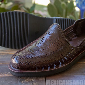 May include: A pair of brown leather sandals with a woven design. The sandals have a closed toe and a thick sole.