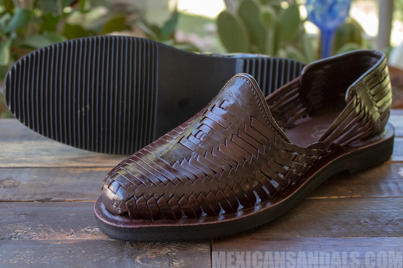 May include: A pair of brown leather sandals with a woven design. The sandals have a closed toe and a thick sole.