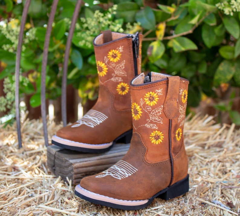 Pu&ograve; includere: Stivali da cowboy in pelle marrone per bambini con cerniera laterale e ricamo di girasoli.