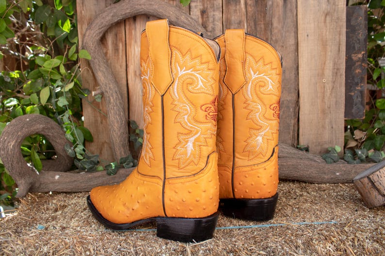 May include: A pair of yellow leather cowboy boots with intricate floral embroidery. The boots have a pointed toe and a stacked heel.