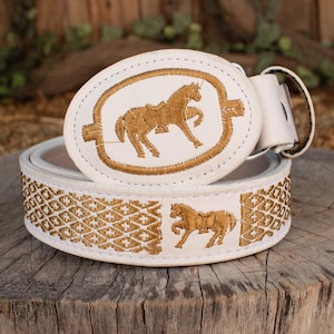 May include: White leather belt with gold embroidered horse and geometric patterns. The belt buckle features a detailed horse design. A stylish accessory for a Western-inspired look.