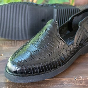 May include: Black leather woven sandals with a closed toe and a black rubber sole. The sandals have a woven pattern and are made of leather.