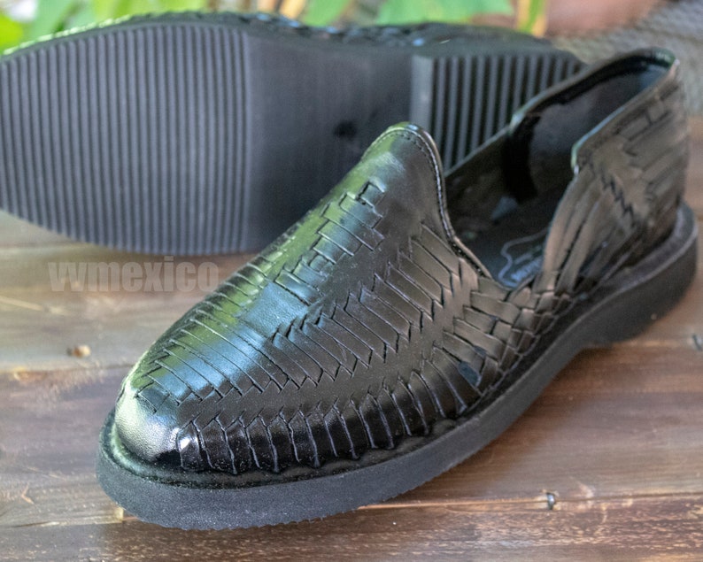 May include: Black leather woven sandals with a closed toe and a black rubber sole. The sandals have a woven pattern and are made of leather.