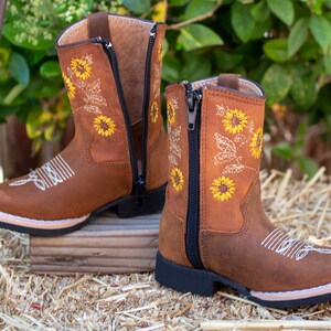 Pu&ograve; includere: Stivali da cowboy in pelle marrone per bambini con cerniera laterale e ricamo di girasoli.
