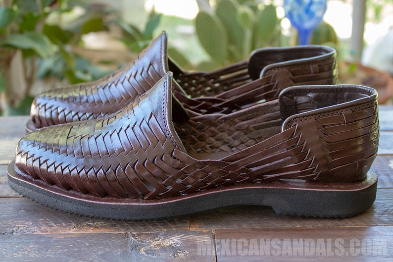 May include: A pair of brown leather sandals with a woven design. The sandals have a closed toe and a flat sole.