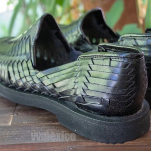 May include: A pair of black leather huarache sandals with a woven design. The sandals have a thick black sole and are made of a soft, supple leather.