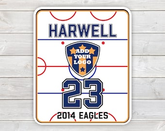 May include: A rectangular sign featuring a white hockey rink graphic with red and blue lines. The text HARWELL appears at the top, a shield with the text ADD YOUR LOGO in the center, the number 23 below, and 2014 EAGLES at the bottom.