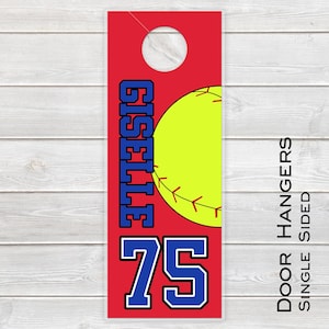 May include: Red door hanger with a softball design. The hanger features the name "GISELLE ELITE" in blue and white, along with the number "75". A yellow softball with red stitching is also visible. The text "DOOR HANGERS SINGLE SIDED" is printed vertically.