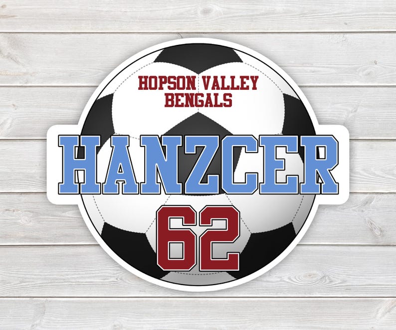 May include: A round sticker featuring a soccer ball design with the text "HOPSON VALLEY BENGALS" in maroon. The name "Hanzcer" is in light blue, and the number "62" is in maroon. The sticker is on a white and gray wood grain background.