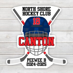 May include: A white sticker with a blue and red hockey helmet with the number 18 on it. The text "North Shore Hockey Club" is above the helmet and the text "Canton" is below the helmet. The text "Peewee B 2024-2025" is at the bottom of the sticker.