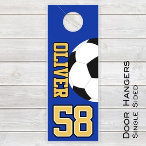 May include: Blue door hanger with a soccer ball and the name "Oliver" in gold letters. The number "58" is also in gold letters. The text "Door Hangers Single Sided" is printed on the right side of the hanger.