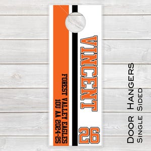 May include: Orange and black door hanger with the text "Vincent" and the number "26". The text "Forest Valley Eagles 10U AA 2024-25" is also on the hanger. The text "Door Hangers Single Sided" is on the right side of the hanger.