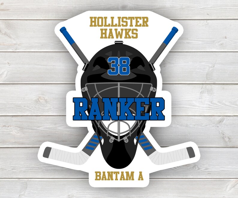 May include: A black and white hockey goalie mask with a blue and white hockey stick crossed behind it. The mask has a black cage and the number 38 on the front. The text "Hollister Hawks" is at the top of the image, "Ranker" is below the mask, and "Bantam A" is at the bottom.
