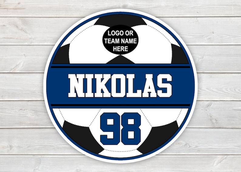 May include: A circular soccer design with a white and black soccer ball pattern. The design includes the name "NIKOLAS" in white block letters on a blue banner, and the number "98" below. The top section has space for a logo or team name.