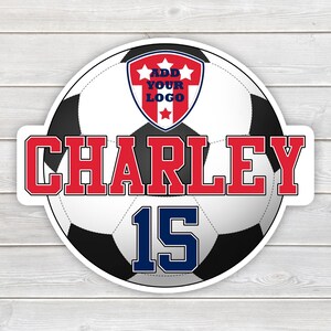 May include: A round sticker featuring a soccer ball design with the name "CHARLEY" in red block letters. The number "15" is in blue. A red, white, and blue crest at the top reads "ADD YOUR LOGO". The sticker is on a white wood grain background.
