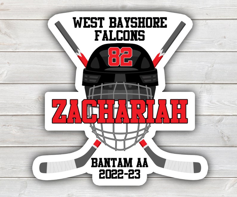 May include: A white hockey sticker with a black and red hockey helmet, two crossed hockey sticks, and the text "West Bayshore Falcons", "Zachariah", "82", "Bantam AA", and "2022-23".