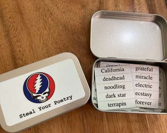 May include: A silver tin with a Grateful Dead logo and the text "Steal Your Poetry". The tin is open and contains small white cards with words such as "California", "deadhead", "noodling", "grateful", "miracle", "electric", "dark star", "ecstasy", "terrapin", and "forever" printed on them.