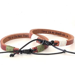 Puede incluir: Dos pulseras de cuero marrón con detalles de cuerda verde y blanca. Una pulsera está grabada con el texto "Do or Do Not, There" y la otra está grabada con el texto "i love ya so much nic. -a".