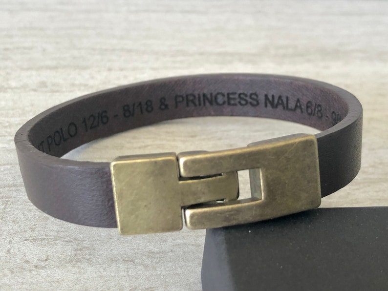 May include: A brown leather bracelet with a brass clasp. The bracelet is engraved with the text "T POLO 12/6 - 8/18 & PRINCESS NALA 6/18 - 9/18".