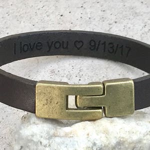 May include: A brown leather bracelet with a brass clasp. The bracelet is engraved with the text "I love you &hearts; 9/13/17".