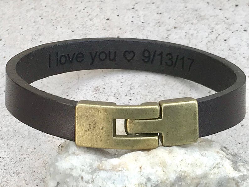 May include: A brown leather bracelet with a brass clasp. The bracelet is engraved with the text "I love you &hearts; 9/13/17".