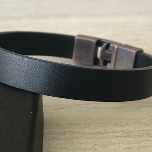 May include: A black leather bracelet with a silver and copper clasp.