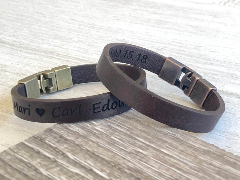 May include: Two brown leather bracelets with metal clasps. One bracelet is engraved with "Mari &hearts; Carl-Edou" and the other is engraved with "09.15.18".