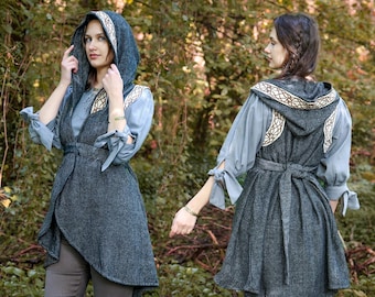 May include: A hooded vest with a long, asymmetrical hemline. The vest is made of a dark blue fabric with a subtle herringbone pattern. The hood is lined with a beige fabric and features a Celtic knot design in gold thread. The vest has a tie at the waist.