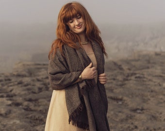 May include: A beige knee-length dress with a horizontal lace trim detail, paired with a dark brown woven shawl featuring fringed edges, dark brown tights, and brown leather lace-up ankle boots. The text Celtic Fusion is visible in the corner.
