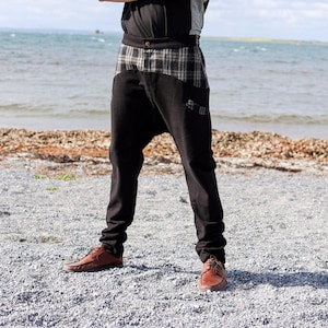May include: Black pants with a plaid panel and a unique design. The pants are worn by a person standing on a beach.
