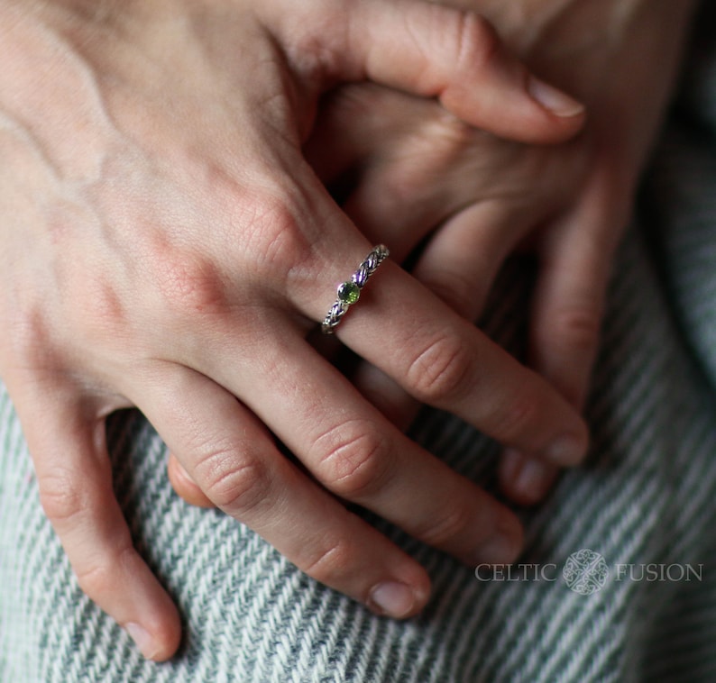May include: A silver ring with a green and purple gemstone setting. The ring is a twisted rope design.