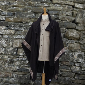 May include: A brown wool poncho with a brown and white patterned trim. The poncho is draped over a mannequin and has a hood.