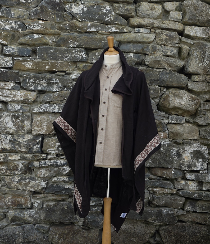 May include: A brown wool poncho with a brown and white patterned trim. The poncho is draped over a mannequin and has a hood.