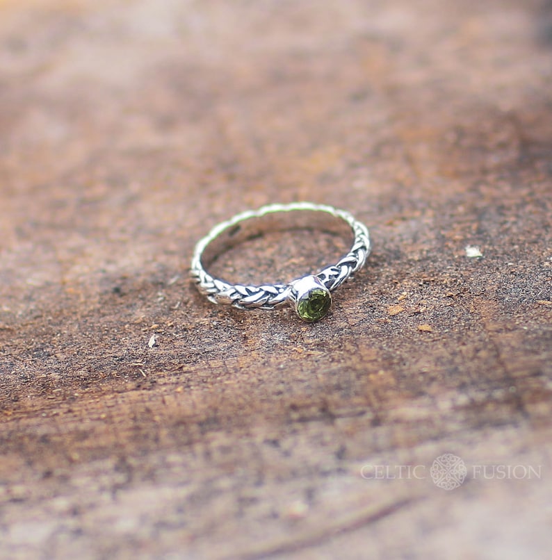 May include: A silver ring with a braided band and a green gemstone. The ring is on a wooden surface.