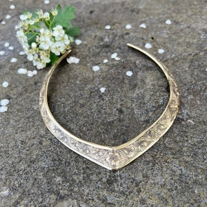May include: A gold-toned metal choker necklace with a floral design. The necklace is on a grey textured surface.