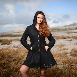 Peut inclure: Un manteau noir à capuche avec une longue jupe fluide et des boutons. Le manteau est porté par une personne aux cheveux longs et roux debout dans un champ.