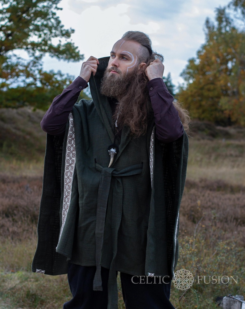 May include: A hooded green cloak with white and brown trim, tied at the waist with a brown belt. The cloak has a Celtic knot design on the trim. The person wearing the cloak has long brown hair and a beard.