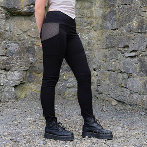 Könnte beinhalten: Schwarze Leggings mit einer großen, gemusterten Tasche an der rechten Hüfte. Die Leggings werden mit schwarzen Plateau-Stiefeln getragen.