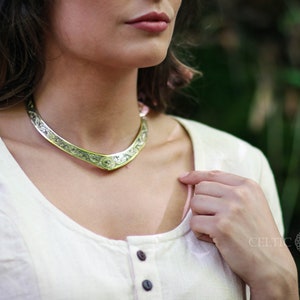 May include: A silver Celtic knot choker necklace with a detailed design. The necklace is worn by a person wearing a white shirt.